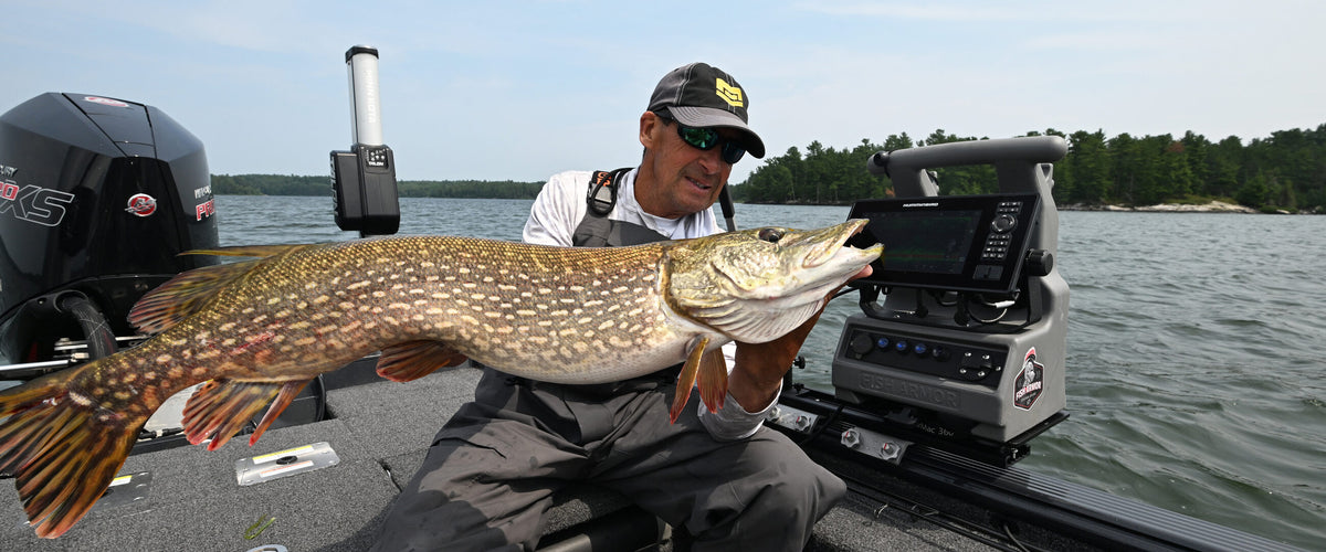 Angler holding a northern pike beside a Fish Armor shuttle mounted on a boat
